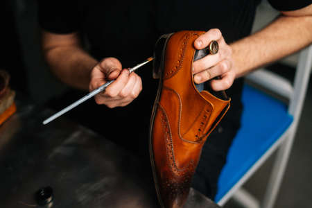 Close-up top view of shoemaker painting heel and sole of light brown leather shoes with brush during restoration working. Concept of cobbler artisan repairing and restoration work in shoe repair shop.の写真素材