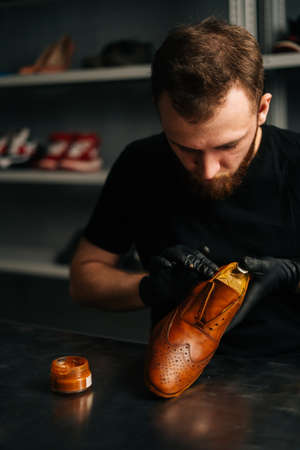 Close-up portrait of shoemaker wearing black gloves rubbing paint on light brown leather shoes with...