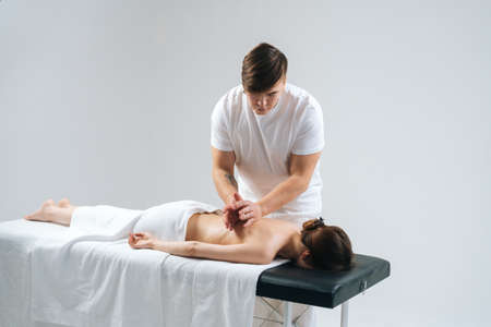 Male masseur tapping the ribs of the palms on the back to young woman in spa salon during massage procedure. Female receiving relaxing back massage. Tapping the back with palms on white background.の写真素材