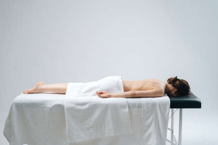 Side view of beauty young woman lying down in spa massage table on white background. Concept of...