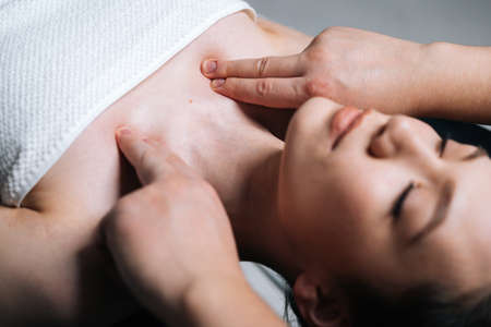 Close-up top view of young woman lying down on massage table with closed eyes during shoulder and neck massage at spa salon. Male masseur professionally massaging shoulders on black background.の写真素材