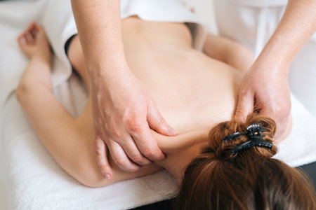 Male masseur with strong hands professionally massaging scapulas and shoulders to female client. Beautiful naked young woman with perfect skin getting relaxing back massage at spa salon.の写真素材