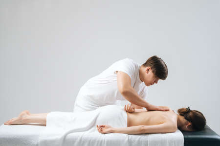 Side view of male masseur with strong hands massaging back of young female lying on massage table on white background. Concept of massage spa treatments.の写真素材