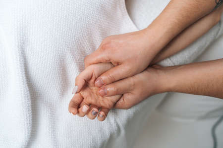 Close-up of male masseur doing finger and palm massage to woman lying on massage table in spa salon. Man physiotherapist doing relaxing massage female on hands, palms and fingers.の写真素材