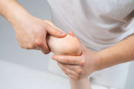 Close-up top view of male masseur massaging feet to young woman lying on massage table. Professional physiotherapist with strong hands performing foot massage. Concept of massage spa treatmentsの写真素材