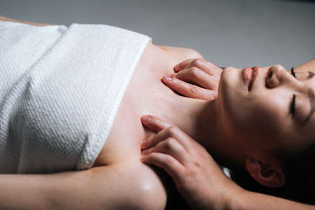 Close-up side view of young woman lying down on massage table with closed eyes during shoulder and neck massage at spa salon. Male masseur professionally massaging shoulders on black background.の写真素材