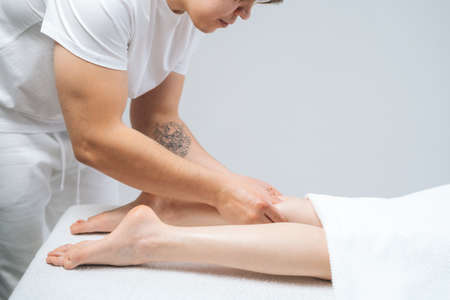 Side view of male masseur massaging lower part of leg to young unrecognizable woman in spa salon. Professional therapist men doing wellness massage shins and legs for female client.の写真素材