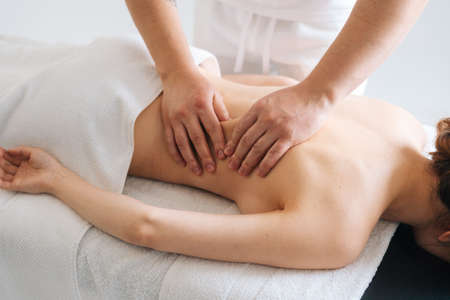 Male masseur massaging back of young unrecognizable woman lying on massage table. Beautiful female with perfect skin getting relaxing massage. Concept of massage spa treatments.の写真素材