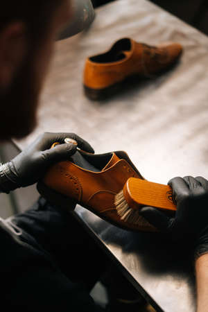 Close-up back view of unrecognizable shoemaker cleaning with brush old light brown leather shoe....