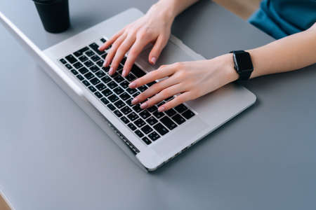 Top close-up view of hands of unrecognizable business woman typing on laptop keyboard sitting at desk with coffee cup in home office, selective focus.の写真素材