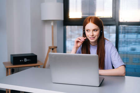 Attractive young woman operator using headset and laptop computer during customer support via phone....