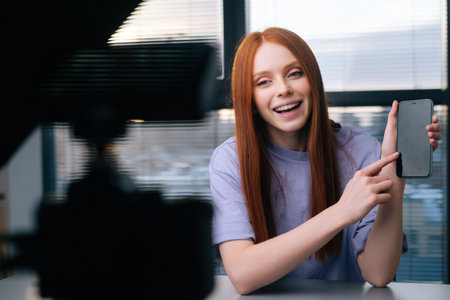 Close-up of smiling young woman blogger talking about new phone using professional camera and...