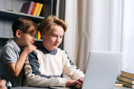 Close-up view of two young little brother watching video on laptop sitting at desk in cozy children room at home. Children using laptop for online learning, happy kids looking at screen.の写真素材