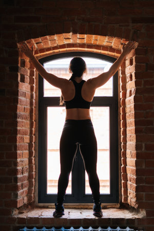 Rear view of muscular young athletic woman with strong beautiful body in sportswear keeping hands...