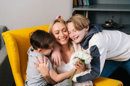 Close-up of two loving cute small kid sons hugging kissing happy young mom congratulating with birthday. Cheerful woman receives gift from child. Concept of family holidays celebration.の写真素材