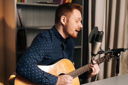 Close-up portrait of guitarist singer man play on acoustic guitar recording sing song using professional microphone stand at home studio. Creative musician having practicing relaxing alone.の写真素材