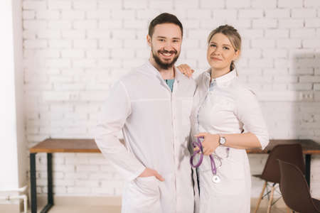 Portrait of two cheerful successful professional doctors wearing white lab coat uniform posing...
