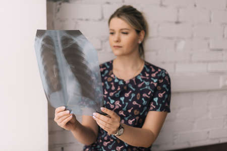 Close-up portrait of frustrated young woman looking on lungs x-ray in sunny day on background of white brick wall, incurable disease, cancer, blurred background, selective focus.の写真素材
