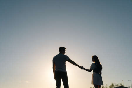 Silhouette of loving young couple dancing at sunset on background of cloudless sky in evening. Happy couple in love having romantic walk outdoors enjoying time together.の写真素材