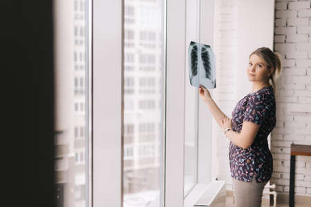 Confident young woman holding image of lungs x-ray in sunny day on background of large panoramic...