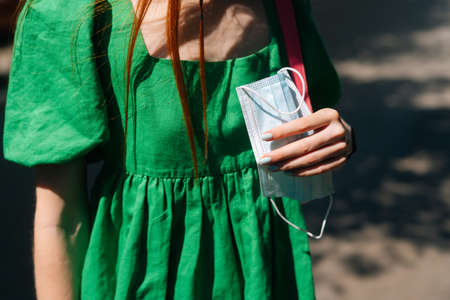 Close-up cropped shot of unrecognizable young woman holding medical protective mask standing at city...