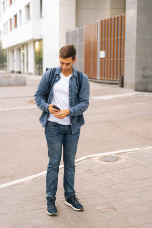 Full length vertical portrait of handsome male courier with thermo backpack using navigation app on...
