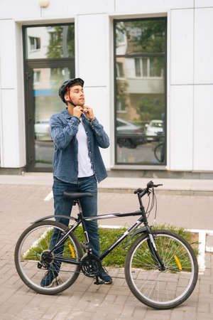 Full length vertical portrait of handsome young man putting helmet on head before going to go ride...