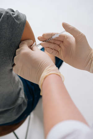 Close-up vertical shot of female doctor in safety medical gloves giving injection vaccine dose in shoulder. Closeup of man getting injected with vaccine in upper arm in isolated white background.の写真素材