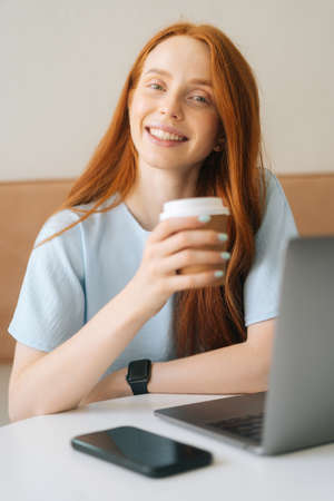 Close-up vertical portrait of happy young beautiful woman holding cup with hot coffee sitting at...