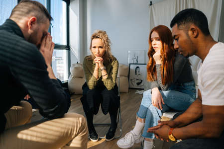 Back view of sad desperate young man telling sad story of mental problem or addiction to other patients sitting in circle. Concept of group consulting of mental health problem with psychologist.の写真素材