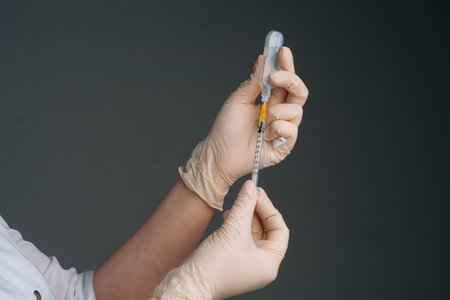 Close-up studio shot of unrecognizable nurse in white gloves holding and filling up vaccine to syringe on black isolated background. Doctor preparing to give injectionの写真素材