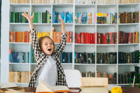 Portrait of excited happy elementary child school girl hands raised up to celebrate the successful mark of education test. Cute primary pupil schoolgirl little girl celebrating after doing homework.の写真素材