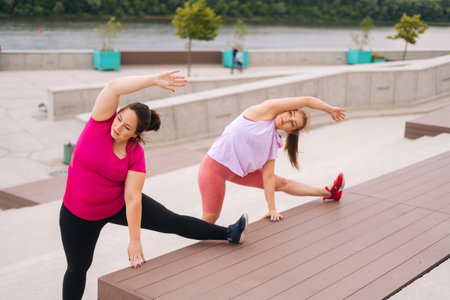 Personal fitness female trainer giving training to overweight young woman helping do tilt to side to stretch muscles outdoor in summer. Instructor help fat woman lose weight.の写真素材