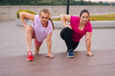 Front view of professional fitness female trainer have personal training with motivated overweight young woman outdoor in summer morning. Instructor help fat woman lose weight outside.の写真素材