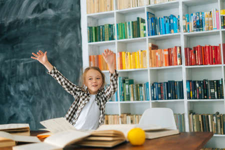 Excited happy elementary child school girl hands raised up to celebrate the successful mark of education test. Cheerful primary pupil schoolgirl little girl celebrating after doing homework.の写真素材