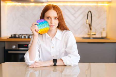 Portrait of attractive redhead young woman holding in hand colorful iridescent soft silicone bubbles...