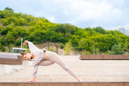 Front view of flexible young yogini woman practicing yoga exercisers on fit mat in summer day...