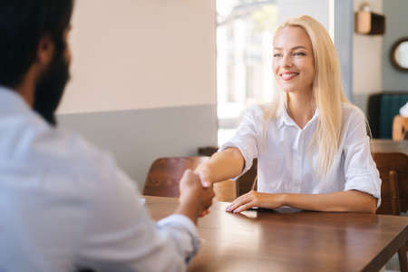Close-up view from back of unrecognizable bearded business man handshaking with cheerful attractive young woman closing deal at business meeting, job interview, agreement business, selective focus.の写真素材