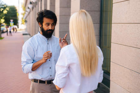 Medium shot from back of unrecognizable business woman and confident Indian business man talking...