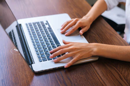 Close-up top view hands of unrecognizable young business woman working online, typing on laptop...