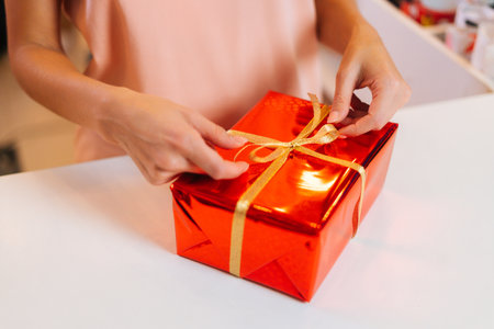 Close-up of unrecognizable female hands holding wrapped Christmas gift box tied golden ribbon and...