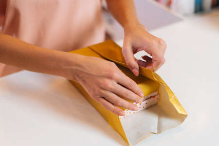Close-up top view of hands unrecognizable young woman wrapping festive Christmas gift box in craft...