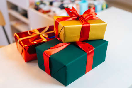 Close-up of some wrapped Christmas gift box tying red and golden ribbons, decorating beautiful bow...