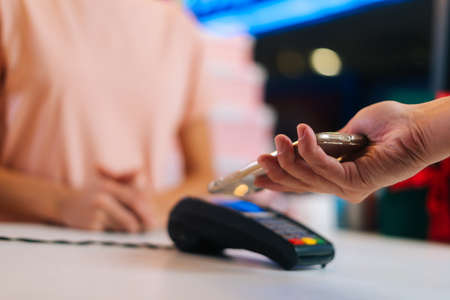 Close-up hands of unrecognizable man paying with NFC technology with smart phone credit card application on POS-terminal, selective focus, blurred background. Contactless payment using smartphone.の写真素材