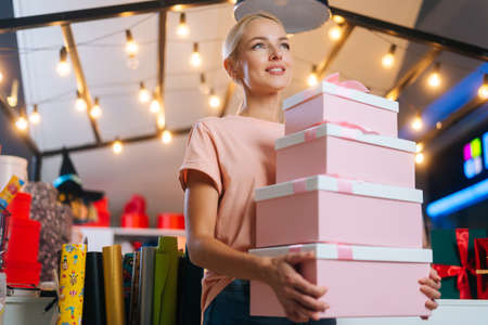 Low-angle view of attractive young woman holding many beautiful Christmas gift boxes on background...