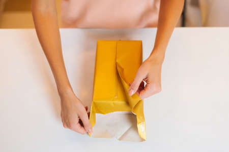 Close-up top view of hands unrecognizable young woman wrapping festive Christmas gift box in craft...