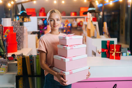 Medium shot portrait of blonde young woman holding many beautiful Christmas gift boxes on background...
