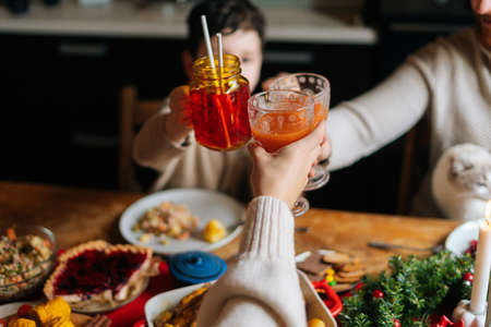Close-up top view to happy young family with adorable little child boy clinking glasses toasting at festive table during holiday family party, selective focus, blurred background.の写真素材
