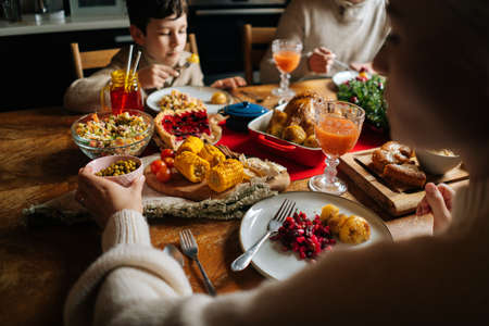 View from back of Caucasian young family enjoying at festive Christmas table during holiday family party. Cheerful mother, father and little son having dinner xmas party, eating and chatting at home.の写真素材