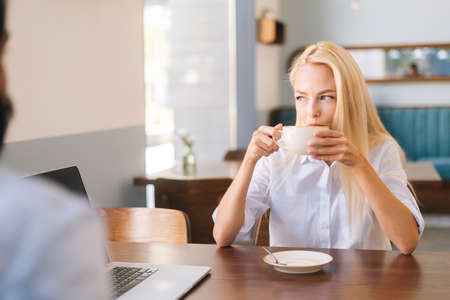 Front view of happy attractive blonde woman sitting in front of unrecognizable young man at table of...